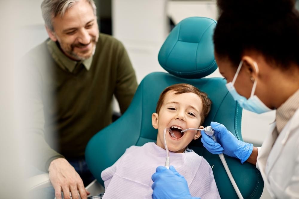 Dental procedure: a graft material is being placed into a tooth socket between two adjacent teeth, with a dental instrument nearby.