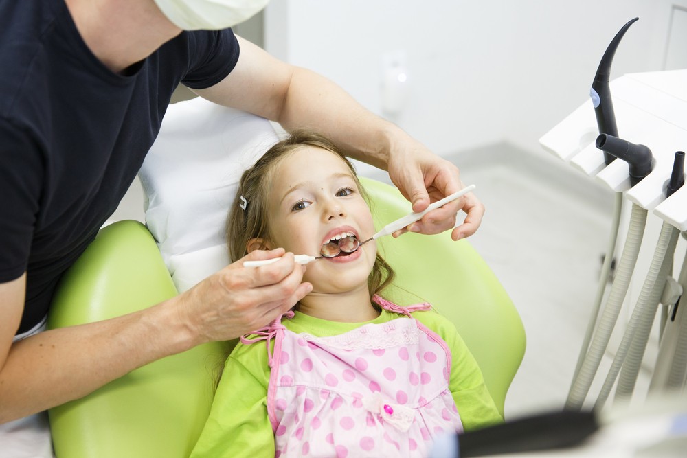 Dentist assisting a young girl as she brushes her teeth in a dental chair.