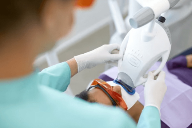 Medical professional in teal scrubs and gloves placing an anesthesia mask over a patient’s face during a procedure.With a patient wearing protective goggles and lying down in a clinical setting, a provider fits an airway mask on the face for anesthesia.
