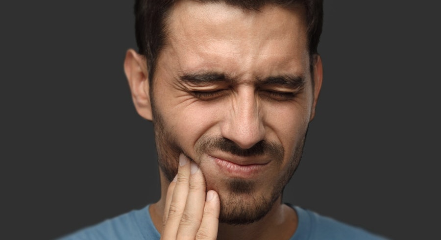 Man grimacing in pain while touching his jaw, suggesting a toothache or jaw discomfort.