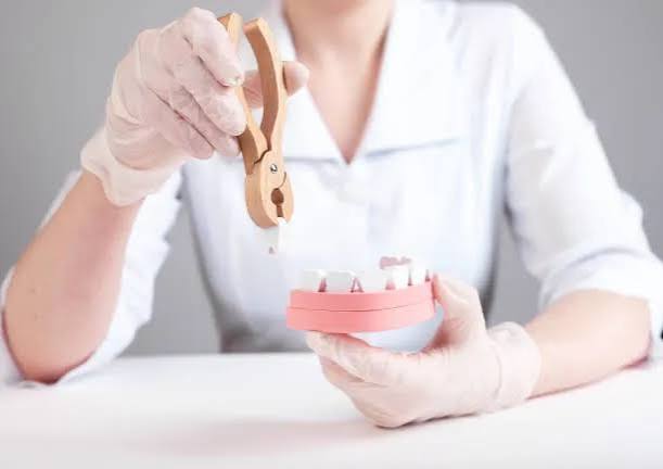 Dental technician wearing gloves adjusts a denture model with pliers at a workbench.