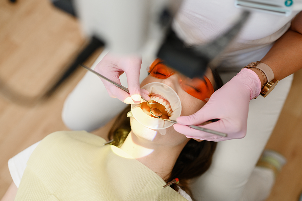 Dentist in pink gloves uses dental tools on a patient reclining in a chair during a dental procedure.