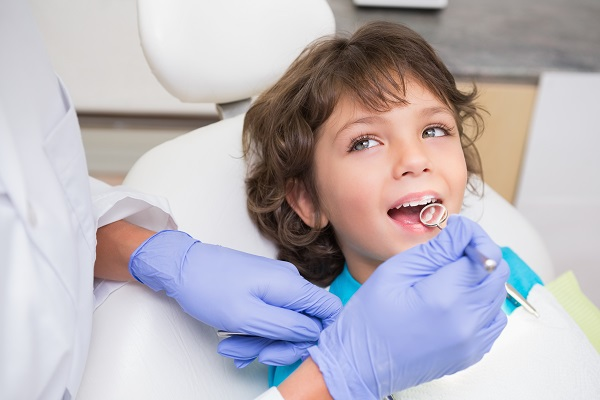 Child patient in a dental chair opening mouth as a dentist in blue gloves examines teeth with a mirror tool
