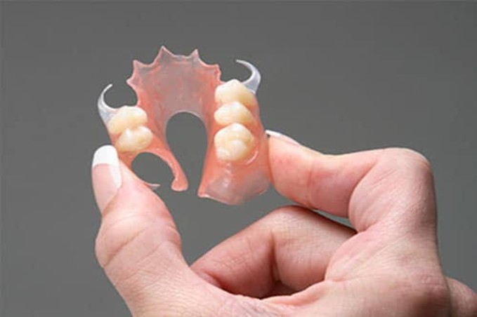 flexible denture 1 - The Smile Connect Partial denture broken into two pieces held between fingers, showing pink acrylic and teeth pieces.